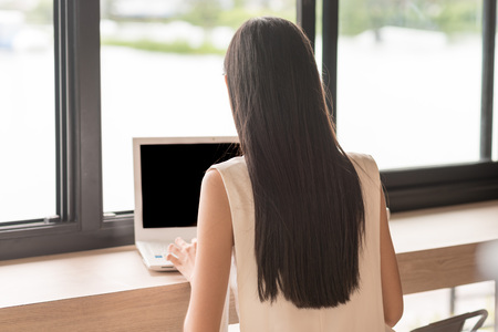 Back side of woman sitting and using computer laptop beside the windowsの写真素材