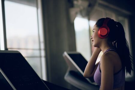 Young asian woman listening music with headphones in the gym.