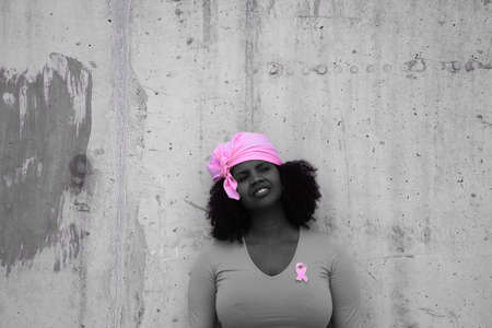 african-american woman with a pink scarf against the fight against breast cancer with a yellow t-shirt making a pose because she has beaten cancerの写真素材