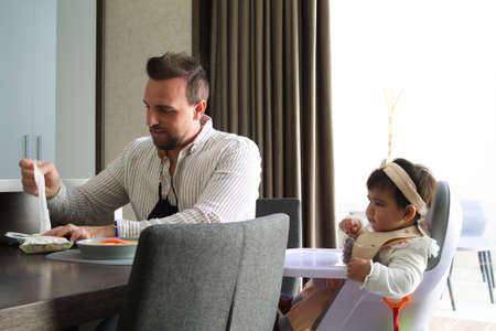 gay father feeding the porridge to the little daughter sitting in his chairの写真素材