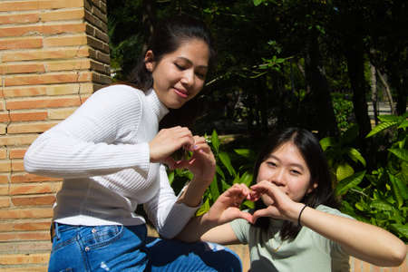 Two Asian women on holiday. They are sitting in a park looking at the pictures on the camera. On her legs she is holding a tourist map of the city. Two young women are happy looking at the picturesの写真素材