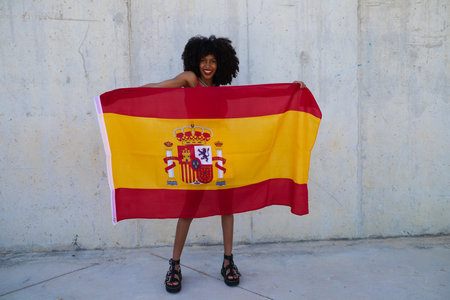 beautiful african-american woman holds the flag of spain in her arms in a photo shoot for a sports publication.の写真素材
