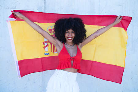 beautiful african-american woman holds the flag of spain in her arms in a photo shoot for a sports publication.の写真素材