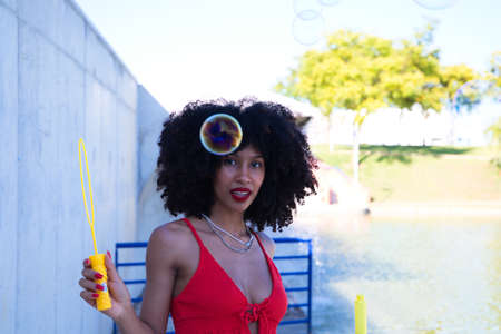 beautiful afro american woman making soap bubbles in the park. The woman is having a great time with the bubbles and that's why she is smiling at the camera. Concept of happinessの写真素材