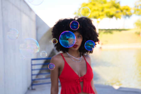 Beautiful afro american woman playing with soap bubbles. The woman is blowing the bubbles and hides among the soap bubbles. Happiness conceptの写真素材