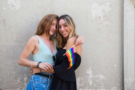 Beautiful young women are hugging each other with a gay pride flag in their hand. The girls are lesbians and are demanding equality between people of the same sex. Concept of equality and diversity.の写真素材