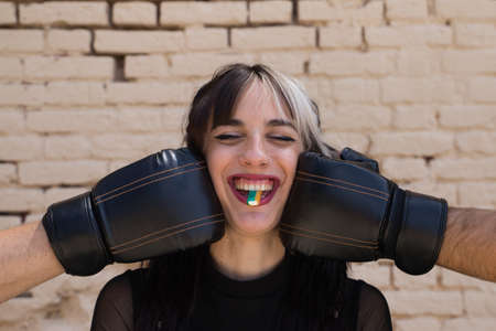young and beautiful girl with a punky tendency. She is wearing boxing gloves and is punching herself in the face. The girl is doing different poses looking at the camera while having fun.の写真素材