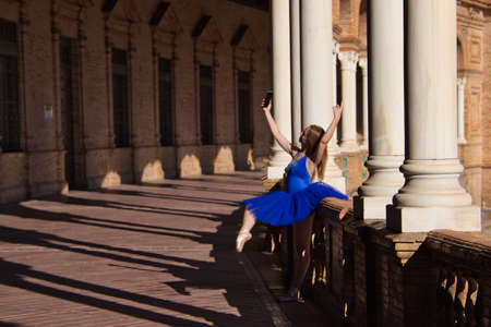 Classical ballet dancer taking a photo with her mobile phone on the railing of a park balcony. The dancer is in rehearsal for a ballet performance and is resting.の写真素材