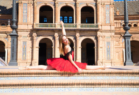 classical ballet dancer in red tutu with her legs open on the steps of a park and her arms outstretched. Classical ballet.の写真素材