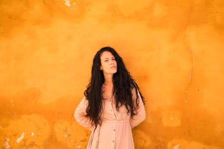 beautiful woman with dark curly hair leaning against the wall and the window grille of a typical Mediterranean style house. The woman is serious and sad. Concept expressions.の写真素材