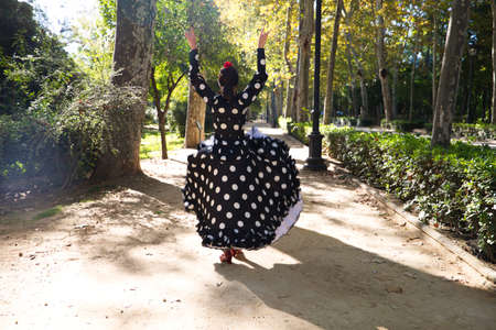 Spanish, beautiful, brunette flamenco dancer with a typical flamenco dress in black with white polka dots. She is dancing in the park in Seville. Flamenco concept cultural heritage of humanity.の写真素材