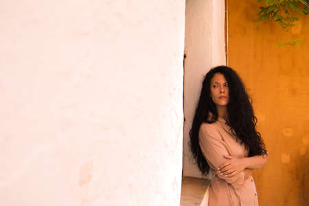 Portrait of beautiful latin woman, brunette and curly hair with the background of an orange wall in Seville making different gestures and expressions with her face. Concept different expressions.の写真素材