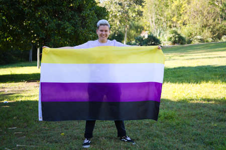 gender non-binary person holds the non-binary pride flag in his hands. He is looking at the camera. Concept of non-binary and androgynous. Diversityの写真素材