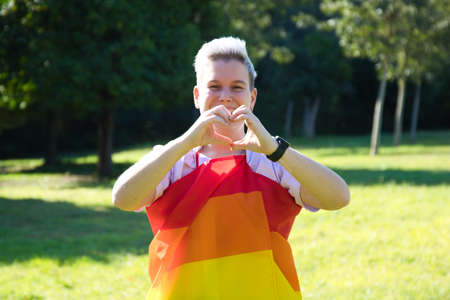 gender non-binary person is rolled up with the gay pride flag on his body. She is looking at the camera. Concept of non-binary and androgynous. Diversity and gay pride.の写真素材