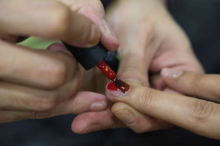Manicure. Close-up of beautiful woman hands polishing nails with red nail polish in beauty salon. Close-up of beautician hand painting client's nails. Beauty concept. High Resolutionの写真素材
