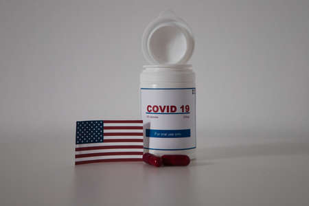 Covid19 pill bottle with several pills outside the bottle and US flag on a lab bench. Concept of the new antiretroviral treatment pill Covid-19.の写真素材