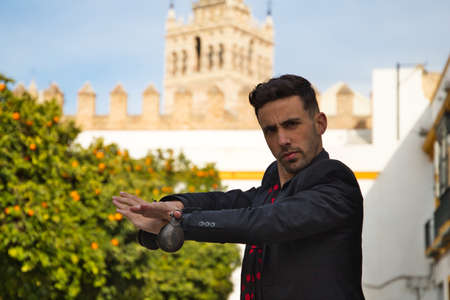 gypsy man dancing flamenco, dressed in black with castanets is posing with his arms up among orange trees and in the background the giralda of seville. Flemish cultural heritage of humanity.の写真素材