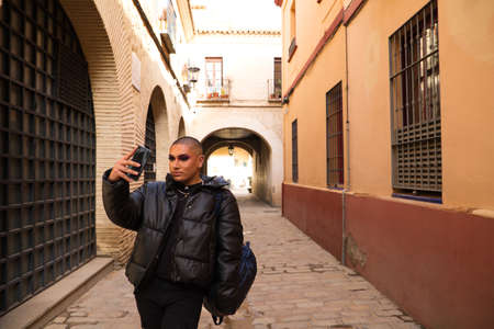 Non-binary and young person from South America is on holiday in Europe, the person is make up and wearing black clothes. He is visiting the city and takes pictures with his mobile phone. Travel.の写真素材