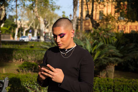 Non-binary and young person from South America is on holiday in Europe, the person is make up and wearing black clothes. He is walking around the city consulting his mobile phone. Concept of equality.の写真素材