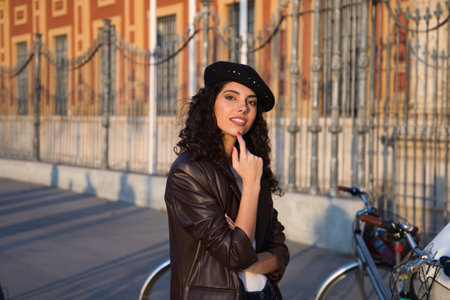 Young, beautiful woman with dark, curly hair gesturing to the camera. She is sightseeing in front of a monument and you can see a bicycle in the background. Holiday and tourism concept.の写真素材
