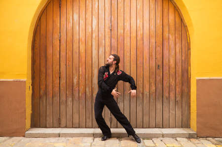 man dancing flamenco with black shirt and red roses, on a background of a wooden door, doing different postures while dancing. Flamenco dance concept cultural heritage of humanity. Feel of passion.の写真素材