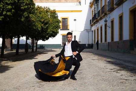 Portrait of young and handsome gipsy man, dressed in black and red shoes dancing with a black and yellow bullfighter's cape in the streets of Seville. Flemish cultural heritage of humanity.の写真素材