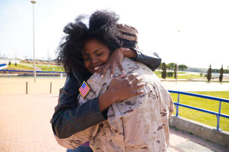 Afro-American woman and American soldier who has just arrived from the war on a peace mission embrace each other tightly. The woman is happy. Concept war and army, peace and mission.の写真素材