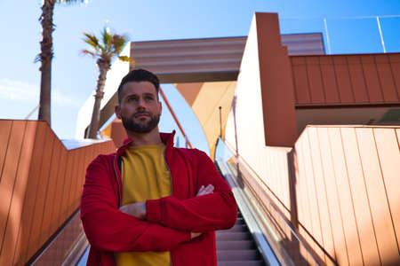 A handsome young man with blue eyes and beard stands next to an escalator in a shopping mall. The man makes different poses and expressions for the photos. Conceptual expressions and gestures.の写真素材