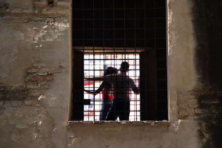 Couple are climbing on a window of an abandoned building. The couple can be seen through the bars.の写真素材