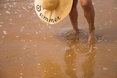 Detail of the feet of a woman on the shore of the beach for health problems in the legs. The woman has a hat to protect herself from the sun. Concept health.の写真素材