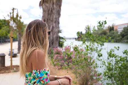 Pretty young blonde woman with sunglasses leaning over the railing of the river. The woman is looking at infinity while smiling or being serious. Various expressions.の写真素材