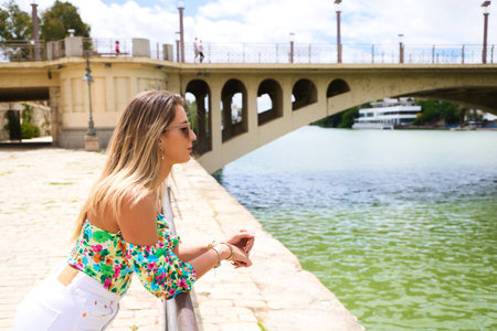 Pretty young blonde woman with sunglasses leaning over the railing of the river. The woman is looking at infinity while smiling or being serious. Various expressions.の写真素材