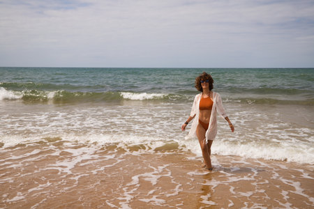 Young beautiful woman in bikini walking along the beach shore. The woman is enjoying her trip to a paradise beach while making different gestures and expressions.の写真素材