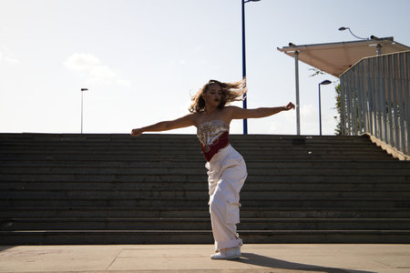 Young and beautiful Latin woman dancing modern dance in the street. In the background steps. Concept dance, hip hop, dance, art, action, beauty, youth art.の写真素材
