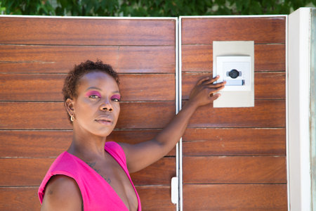 Young, beautiful Afro American woman calling the electronic doorman at the entrance of a luxury flat.の写真素材