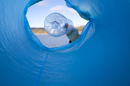 Hands of a garbage collector worker in foreground hold plastic bottles to put them in garbage bag for recycling. Concept, Waste management. Environmental problems. Daily tasks.の写真素材