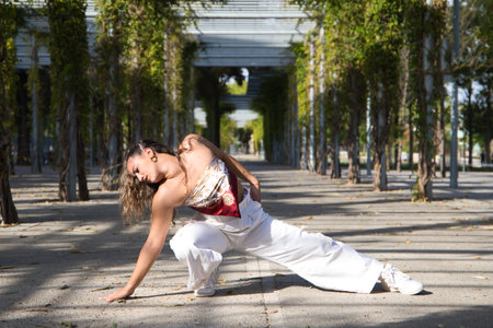Latin woman, young and beautiful dancing modern dance on the street in a park and makes different expressions and postures. Concept dance, hip hop, dance, art, action, beauty, youth art.の写真素材