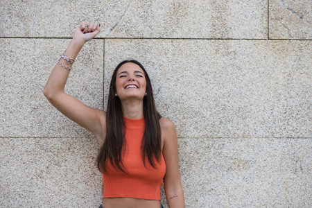 beautiful young woman raises her arms with clenched fists celebrating victory and achievements on gray background.の写真素材