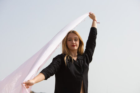 Young and beautiful blonde woman walks along the shore of the beach with a pink sarong in the wind, in the background the sea and the sky. Concept of freedom and holidays.の写真素材