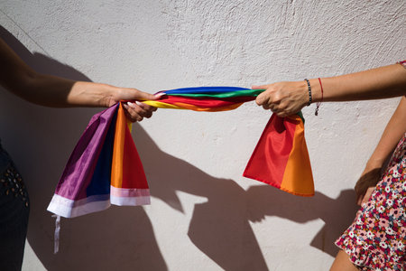 detail of gay flag held at each end by the hands of two lesbian women. Concept gay pride, homosexuality, lesbians, gay pride.の写真素材