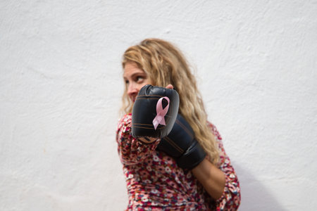 Young beautiful woman with boxing gloves with pink ribbon against breast cancer and white top on white background. Concept claims and world day against cancer.の写真素材