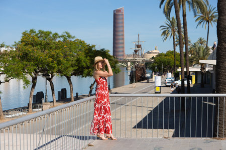 Pretty young blonde woman with straw hat on her head. She is dressed in a white dress with red print and is having fun doing different poses. The woman is on holiday in Spainの写真素材