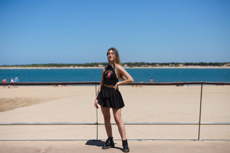 Blonde, young and beautiful woman dressed in black skirt and black top is on the promenade of the sea. The girl is doing different body postures. In the background the blue seaの写真素材