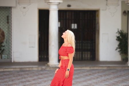 Beautiful young blonde woman from the United States is on a sightseeing trip in Seville, Spain. The girl is happy and visits a square with 18th century columns and arches with frescoes on the wallの写真素材