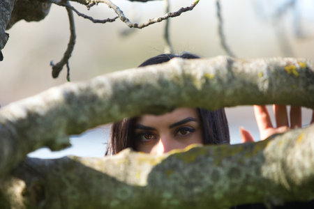 Black eyes of a young girl between the trunks of a leafless treeの写真素材