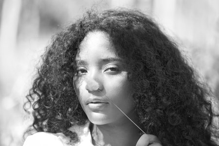 woman, young, brunette with curly hair dressed in white shirt with a dry twig she has picked up in the forest, she passes it over her face. black and white photo, monochromeの写真素材