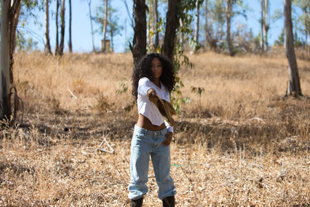 woman, young, beautiful, Latin, brunette with curly hair dressed in white shirt, jeans and boots throws a straw hat spinning as if it were a flying disc. The farmer is among eucalyptus treesの写真素材