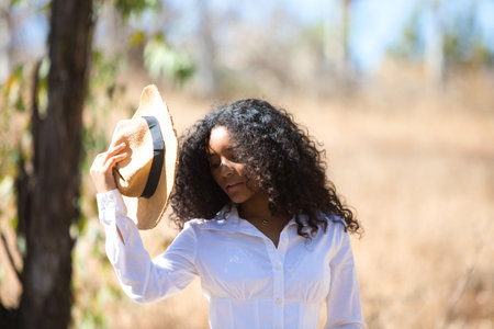 woman, young, beautiful, Latin, brunette with curly hair dressed in white shirt and jeans, puts on a hat with one hand among the eucalyptus trees in the field.の写真素材