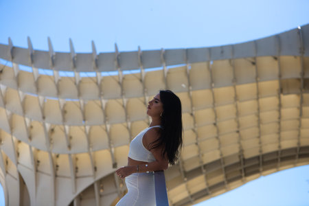 Young Spanish woman, brunette and beautiful in white dress on the railing of the stairs of the square in Seville, Andalusia, Spain. The woman is relaxing and enjoying in the cityの写真素材