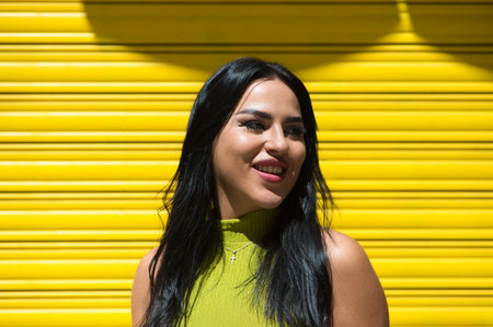 Young Spanish woman, brunette and beautiful with green dress on yellow background smiles and is very happy. Concept happiness and joyの写真素材